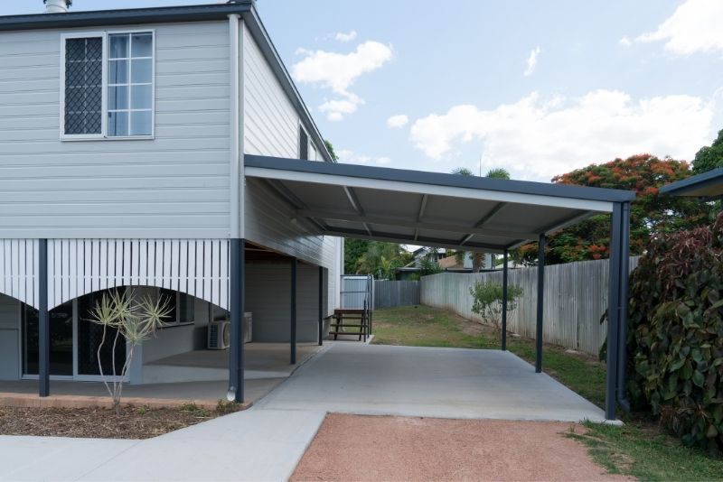 A steel-framed carport attached to a Queenslander home over a concrete driveway