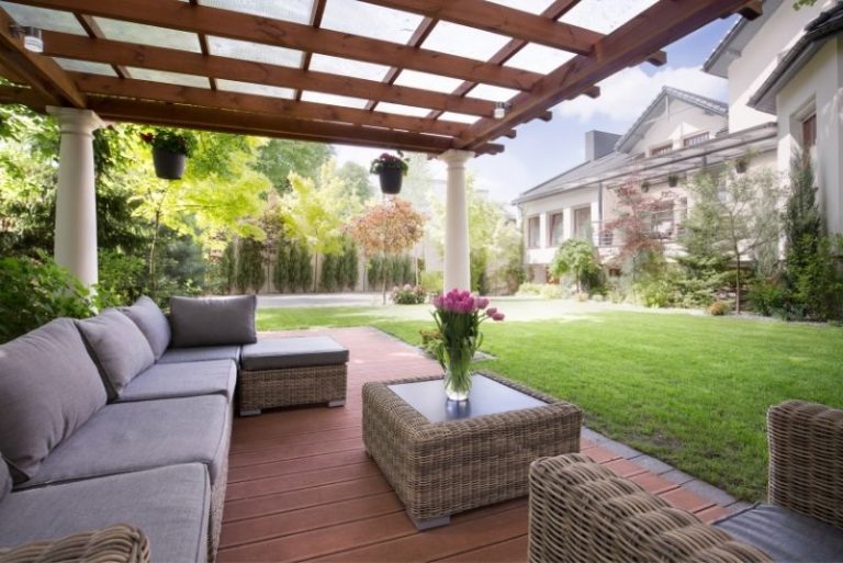 Timber pergola with a slatted roof over an outdoor lounge and dining area in a landscaped backyard