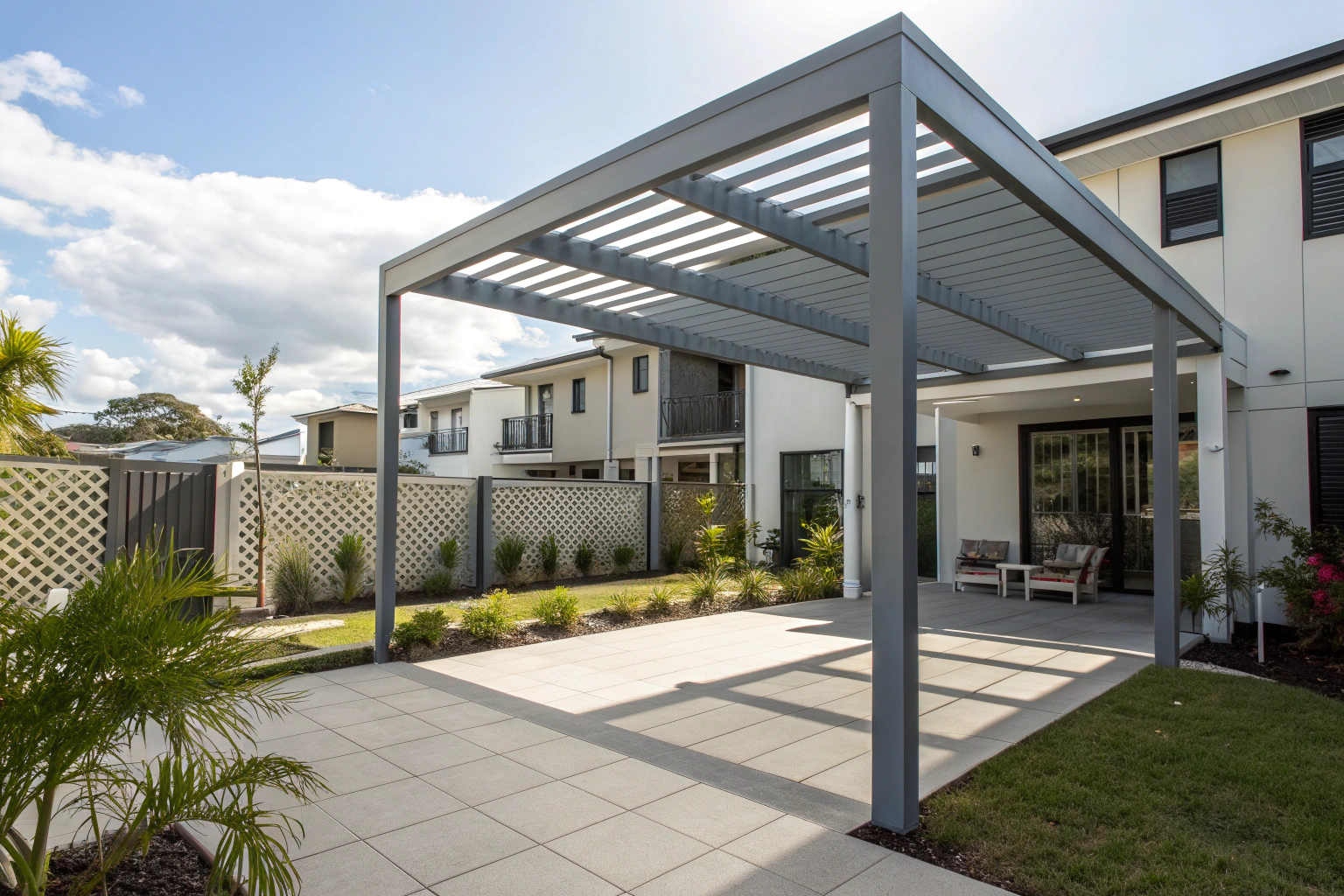 A grey slatted pergola over a paved courtyard in a compact modern backyard